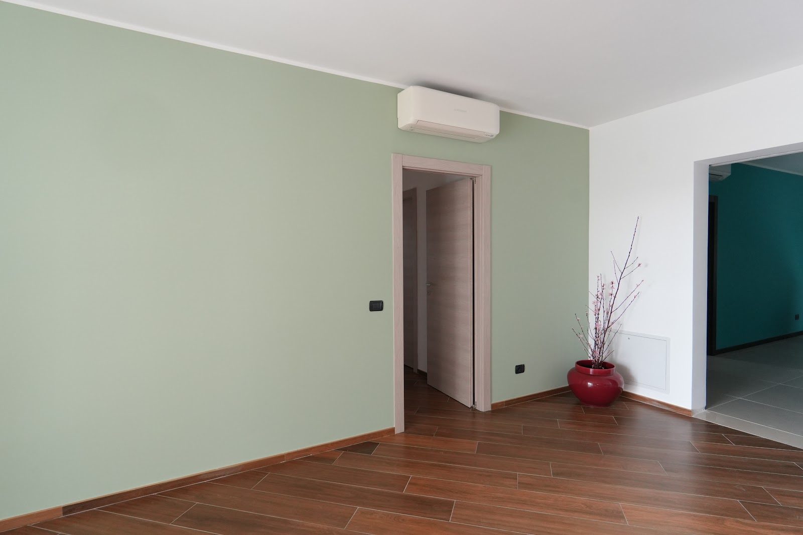 Soggiorno con parete verde salvia e pavimento in parquet